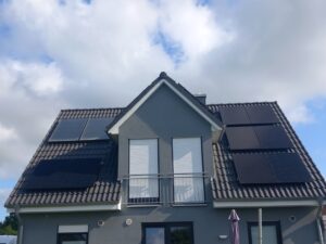 „Frontansicht eines modernen grauen Einfamilienhauses mit Satteldach. Auf beiden Dachflächen sind mehrere schwarze Photovoltaikmodule installiert, die zusammen eine 10 kWp-Photovoltaikanlage bilden.