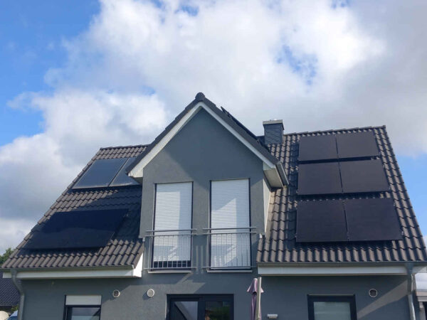 Frontansicht eines zweigeschossigen Einfamilienhauses mit Satteldach und Dachgaube. Auf beiden geneigten Dachflächen sind mehrere rechteckige Photovoltaikmodule dachparallel montiert. Fassade in Grau, mittig zwei Fenster mit Rollläden und französischen Balkonen. Ziegeldach, bewölkter Himmel. Frontansicht eines zweigeschossigen Einfamilienhauses mit Satteldach und Dachgaube. Auf beiden geneigten Dachflächen sind mehrere rechteckige Photovoltaikmodule dachparallel montiert. Fassade in Grau, mittig zwei Fenster mit Rollläden und französischen Balkonen. Ziegeldach, bewölkter Himmel.